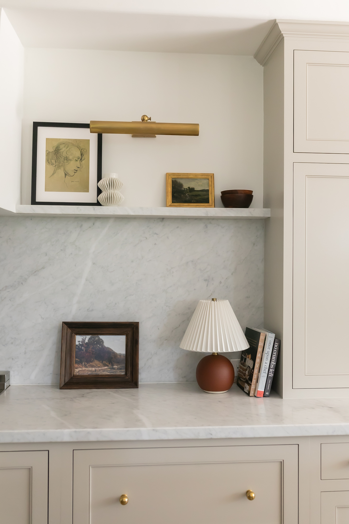 Kitchen nook detail with marble backsplash shelf, brass picture light, and artful decor — J. Arthur Custom Homes