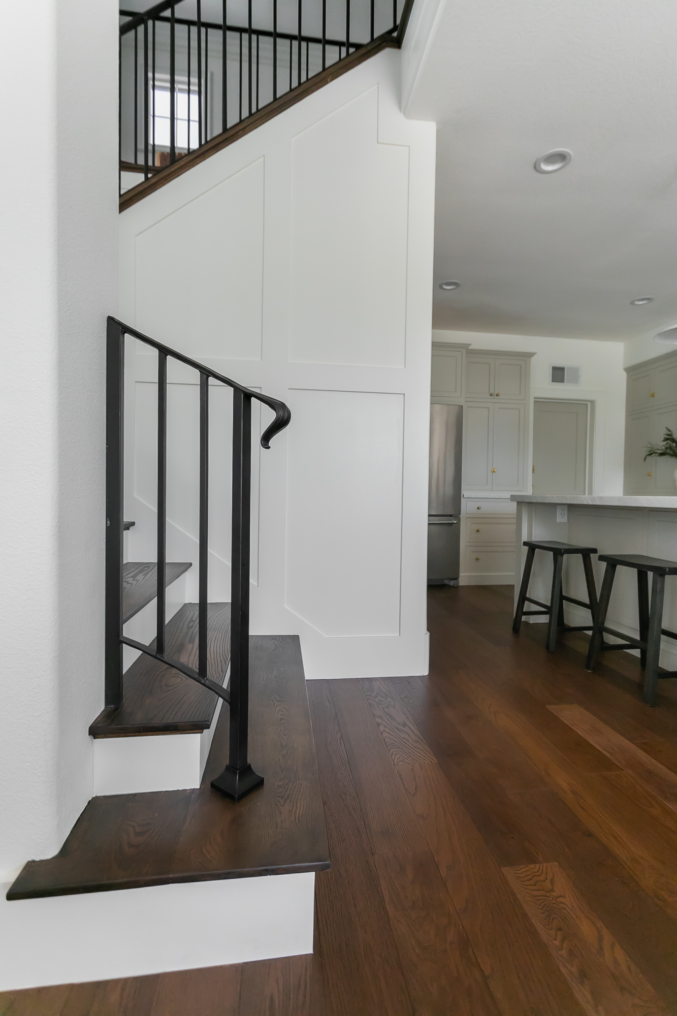 Custom home staircase with black iron railing and dark wood treads, open to kitchen — J. Arthur Custom Homes Boerne TX